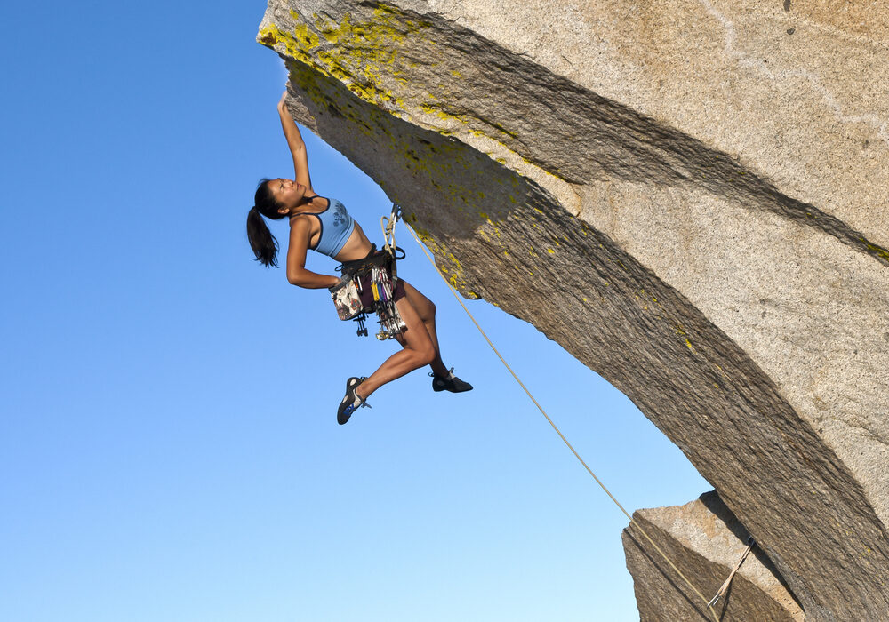 Jonge klimmer hangt met een arm aan rots.