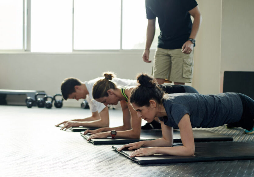 Shot of a group of young people working out on exercise mats while their trainer looks on