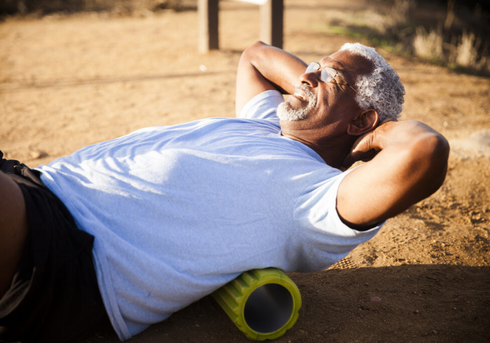 An attractive senior black man gets some back relief by using a foam roller
