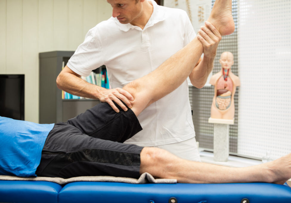 A  doctor, performing Lasegue test at a male patient. This test stretches the nerves of the leg and spine and gives information about the origin of pain.