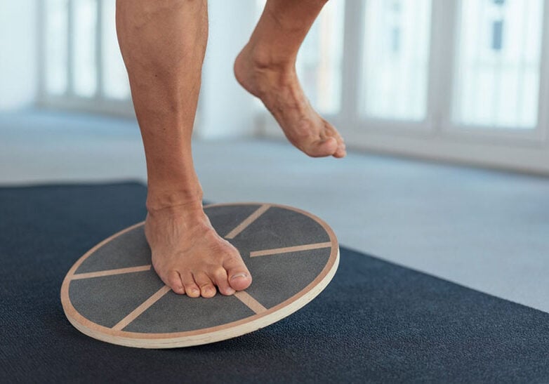 Man strengthening his leg muscles working out using a balance board in a gym in a close up view on his feet and equipment