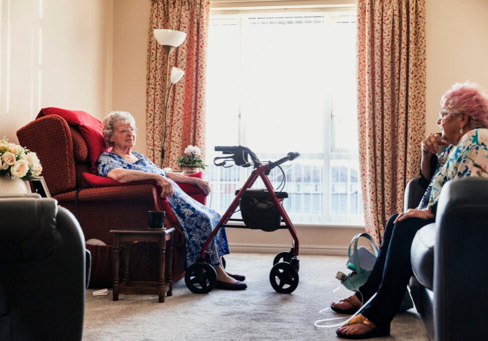 Two senior woman sitting chatting in a nursing home in North East of England. One has pink hair.