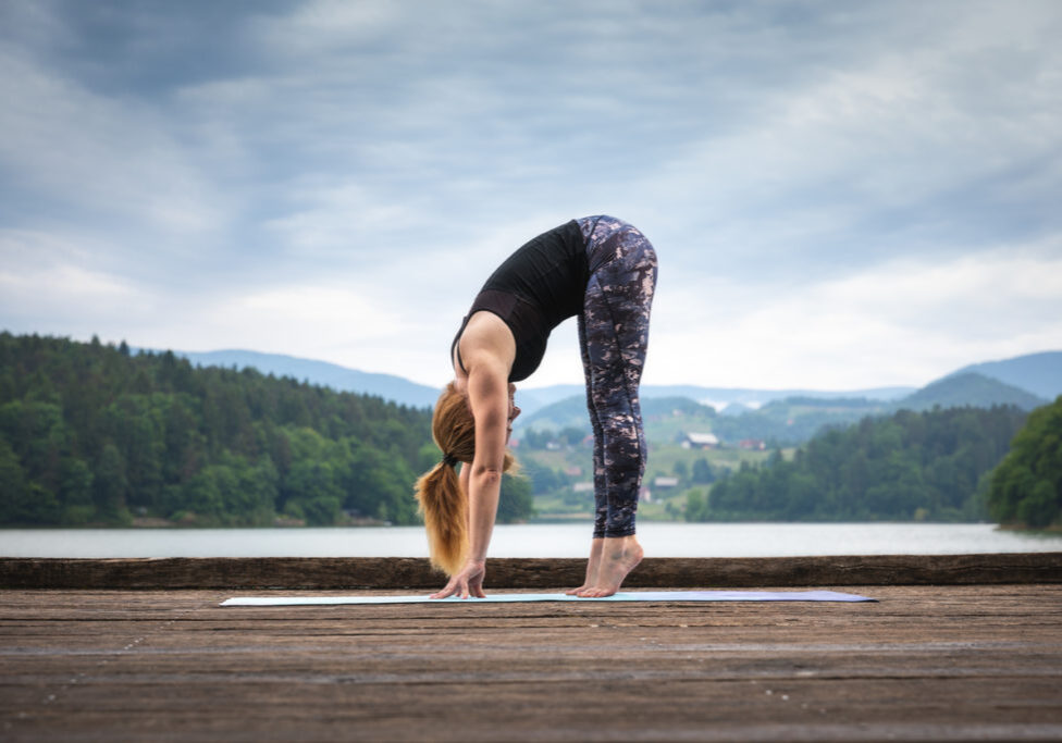 Woman doing yoga on the wooden jetty. Standing Forward Bend.