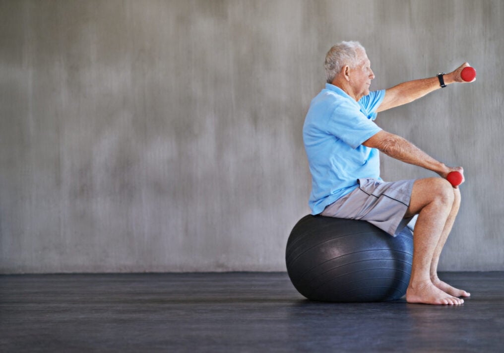 Shot of an elderly man using weights while sitting on a swiss ball