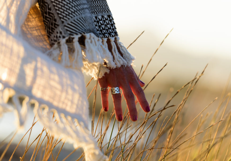 Woman hand caressing grass in nature near the sea at sunset