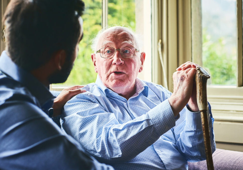 Elderly man with walking stick talking to doctor at home