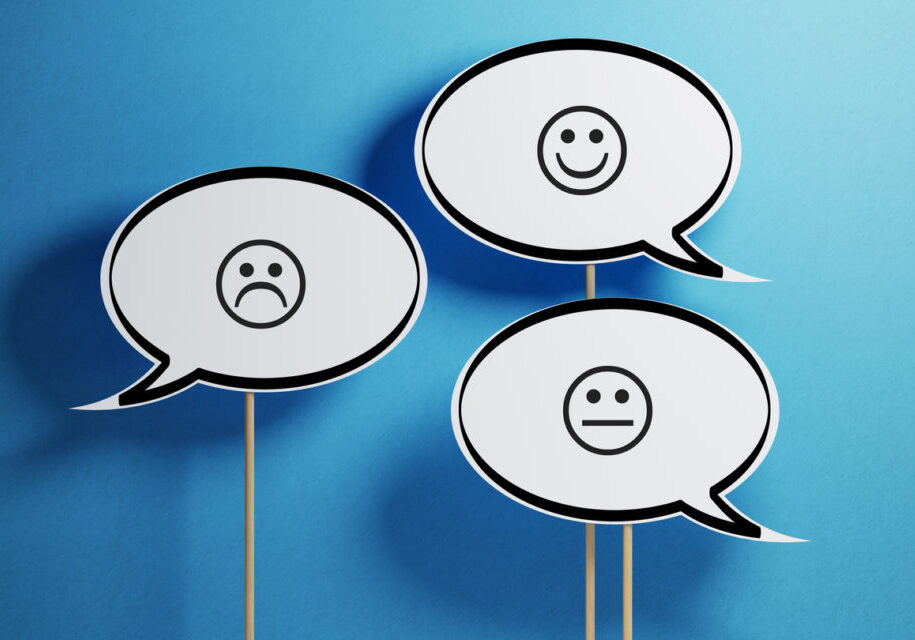 White chat bubble with wooden stick on blue background. There are various smiley faces on the speech bubbles. Horizontal composition with copy space.