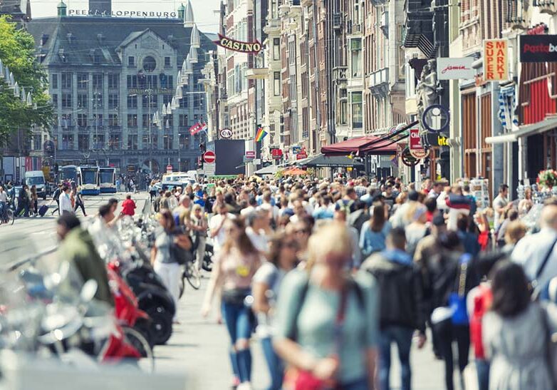 Horizontal color image of a crowded Damrak in Amsterdam. No social distancing applied.