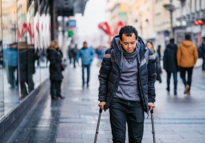 Young mixed raced injured man using walking canes for walking downtown.